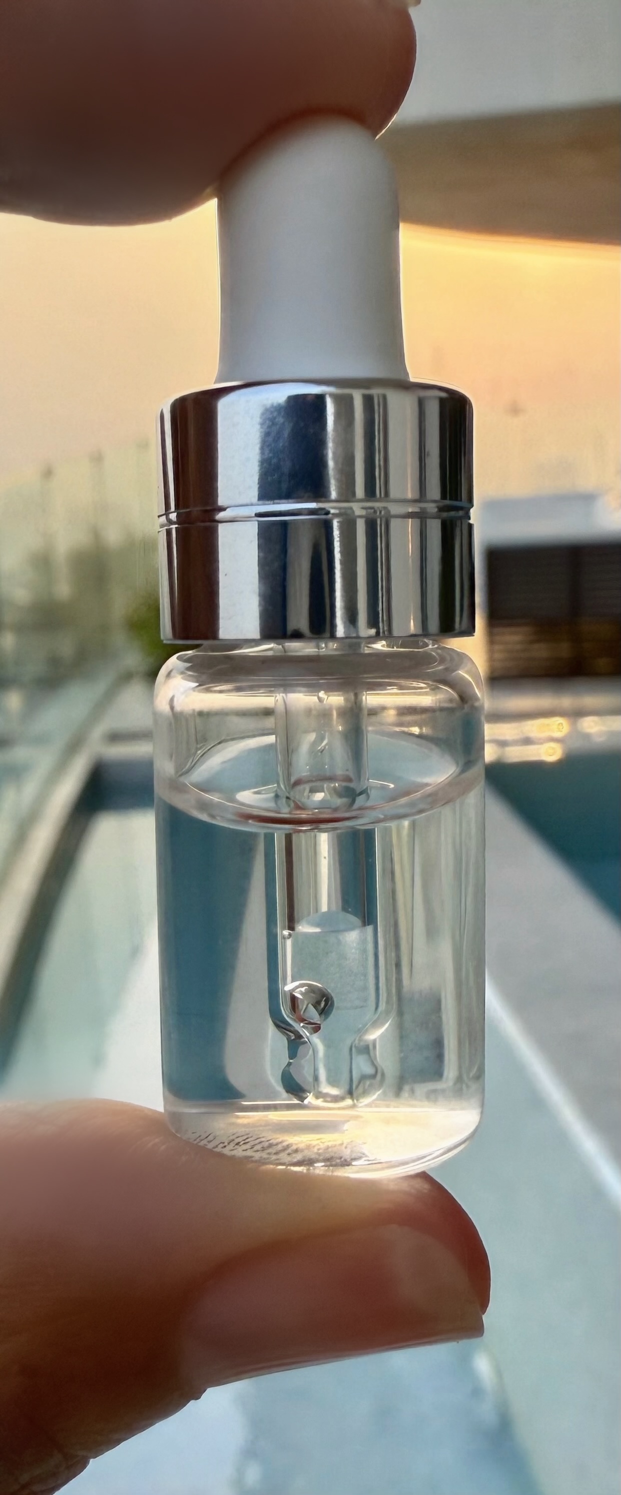 Nahaufnahme eines Glaspipettenfläschchens mit silberner Kappe, klarer Inhalt