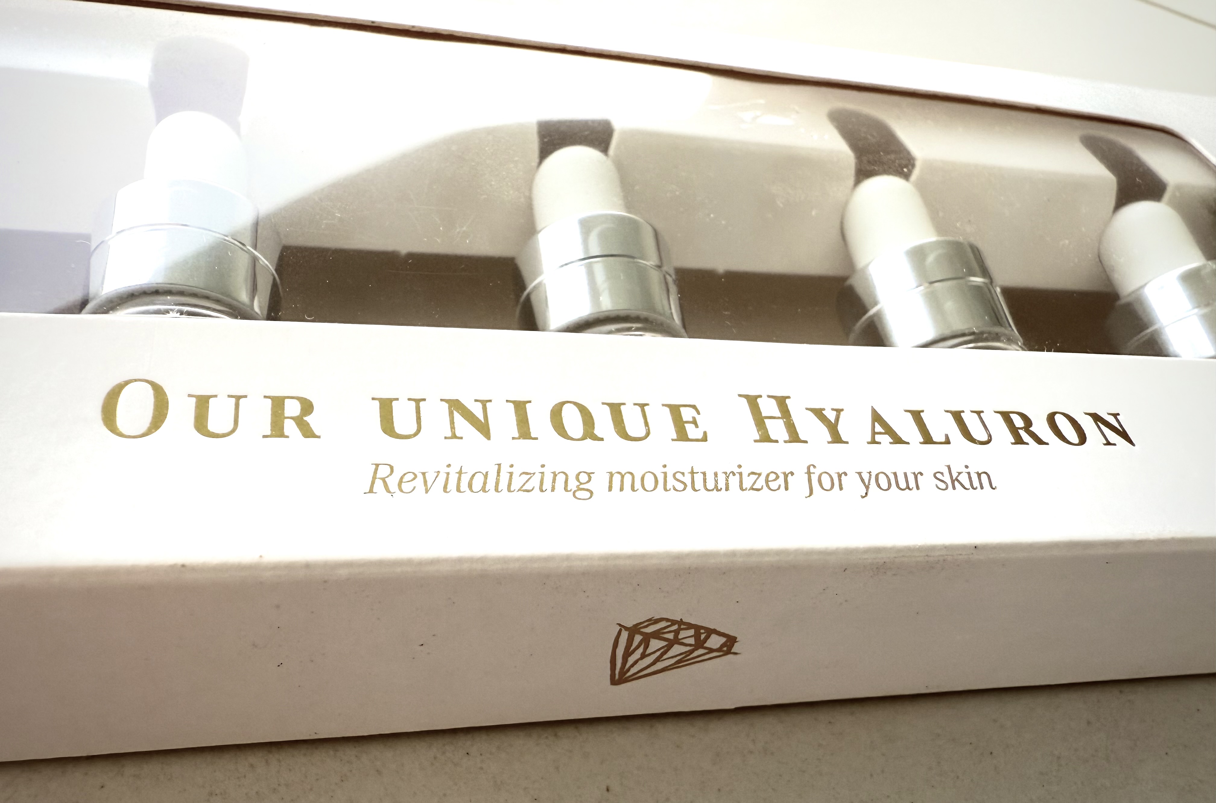 Eine Verpackung mit vier silbernen Tropfflaschen, die Hyaluron-Serum enthalten.