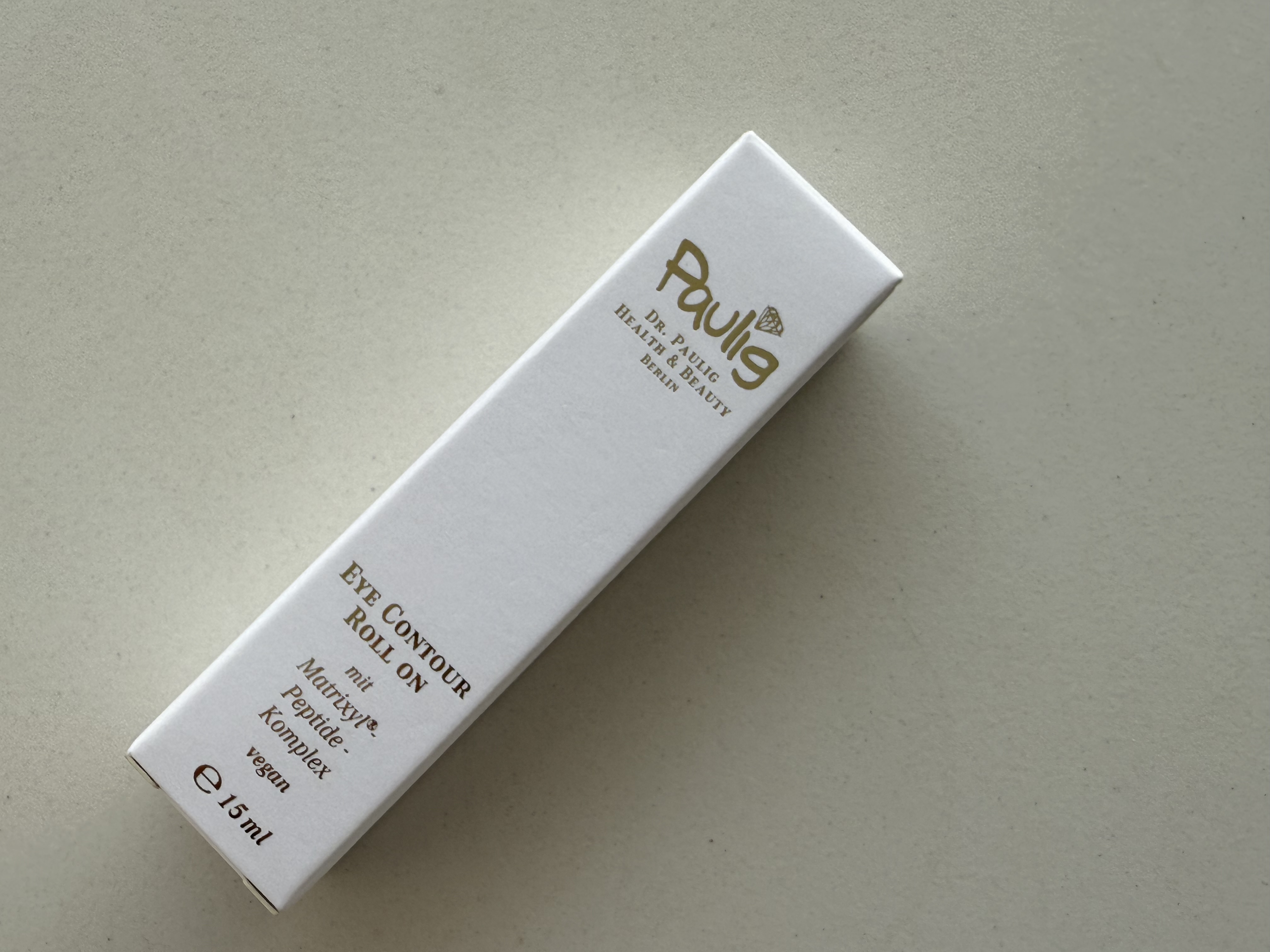Weiße Schachtel mit schwarzer Aufschrift "Eye Contour Roll On" auf beigem Hintergrund